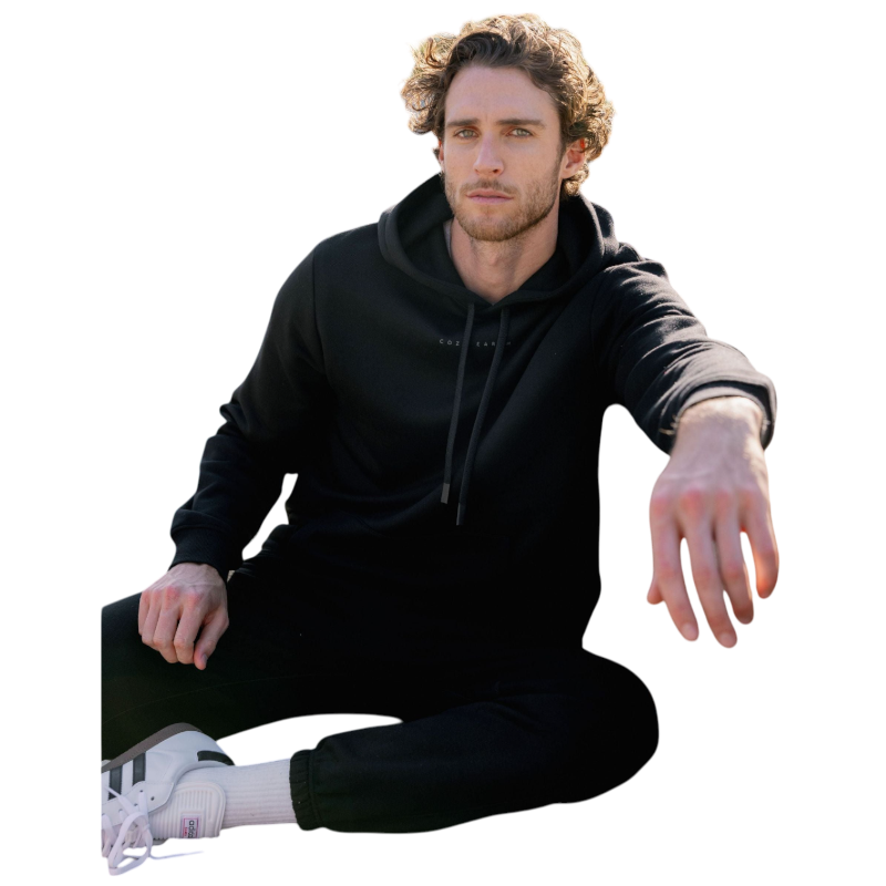 A person with curly hair is wearing a Cozy Earth Men's CityScape Hoodie in dark green and standing against a plain white background, with their hands together. |Color:Spruce