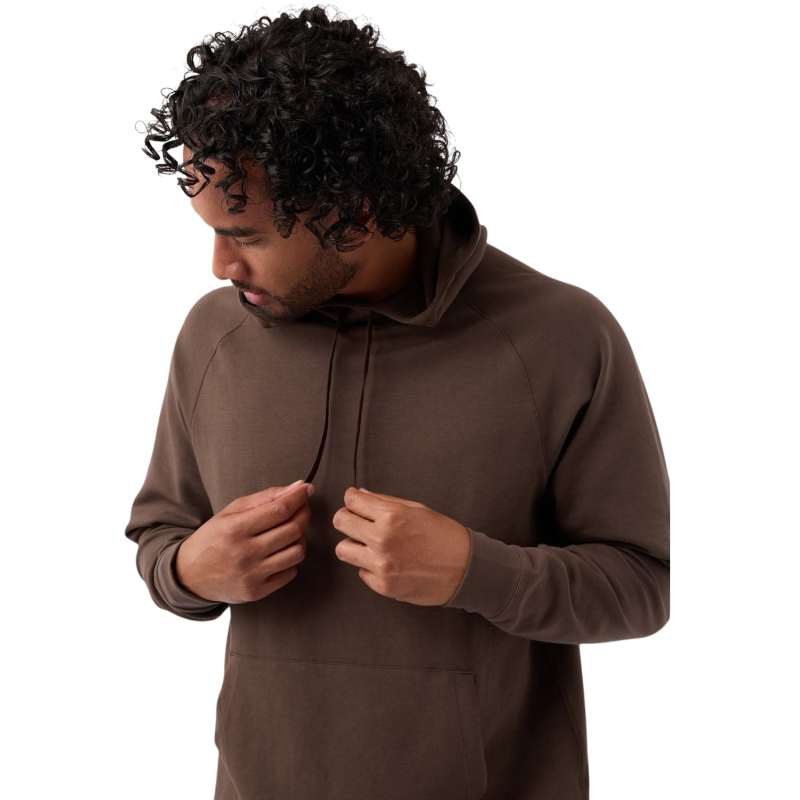 A person with curly hair is looking down and adjusting the drawstrings of their brown Men's StretchTech Hoodie from Cozy Earth. They are wearing a casual outfit and standing against a plain white background. |Color:Cacao