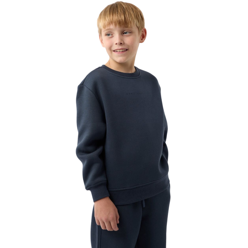 A young boy with blond hair is wearing the Cozy Earth Kid's CityScape Crewneck sweatshirt along with matching pants. He is standing, smiling, and looking slightly to the side against a plain white background. |Color:Eclipse