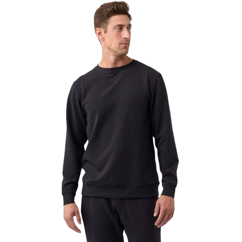 A man with short brown hair, dressed in a Cozy Earth Men's StretchTech Crewneck and black pants, stands against a plain white background. He is looking slightly to his right, with his hands relaxed at his sides. |Color:Jet Black