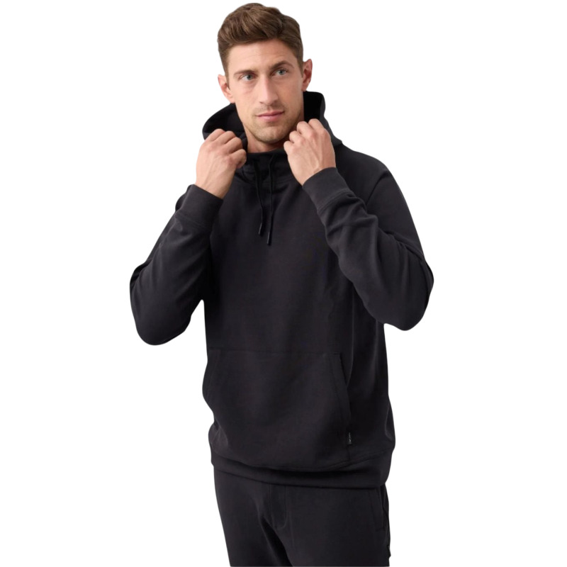 A man standing against a plain white background is wearing a black Men's StretchTech Hoodie and black pants from Cozy Earth. He is holding the hoodie strings with both hands. The man has short brown hair and a serious expression. |Color:Jet Black