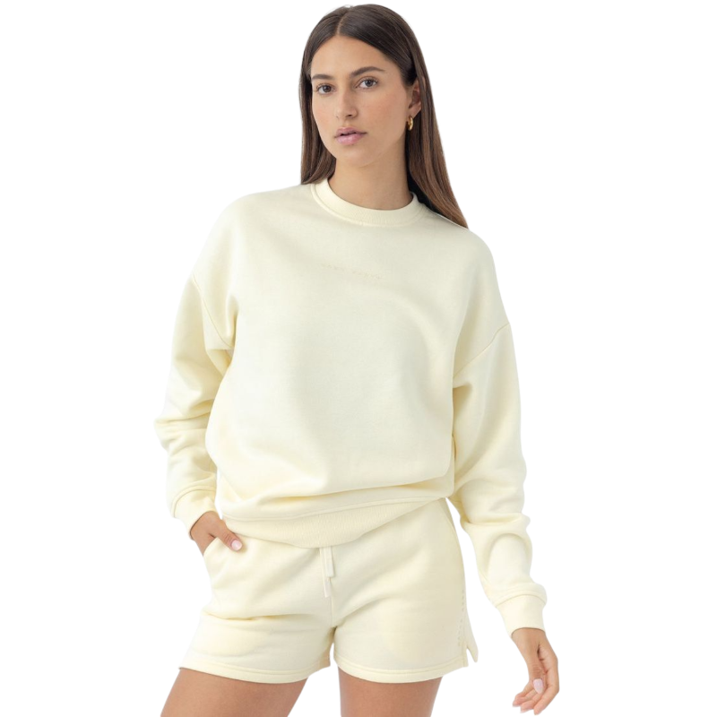A woman with long brown hair wears a Cozy Earth Women's CityScape Crewneck and matching shorts against a plain white background. She has a neutral expression and keeps one hand in her pocket. |Color:Lemonade