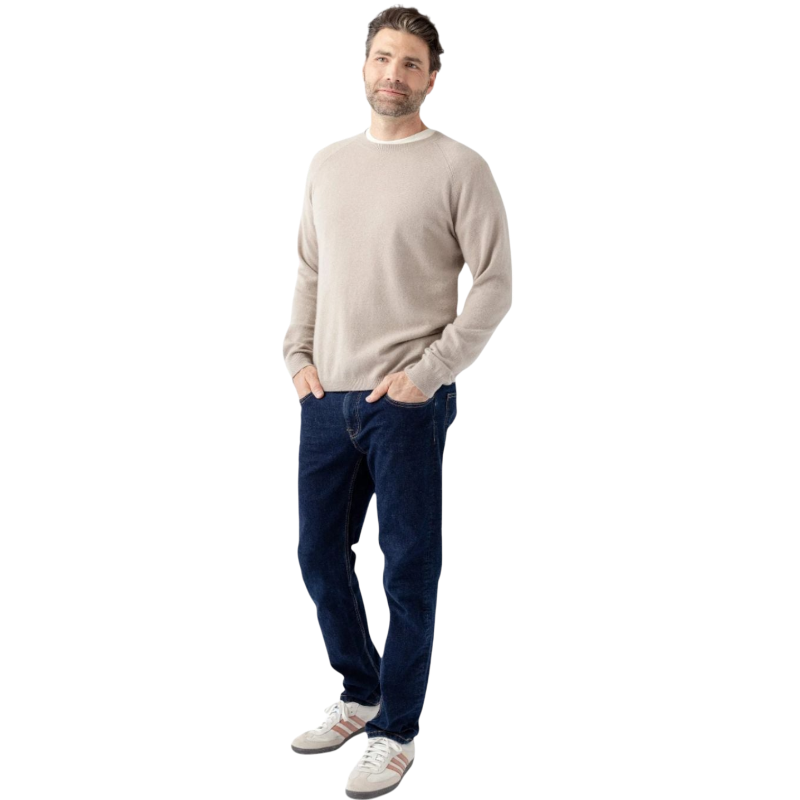 A man stands against a white background wearing a Men's Crewneck Sweater by Cozy Earth, dark blue jeans, and gray sneakers with white and red accents. He has his hands in his pockets and is smiling slightly at the camera. |Color:Sandstone