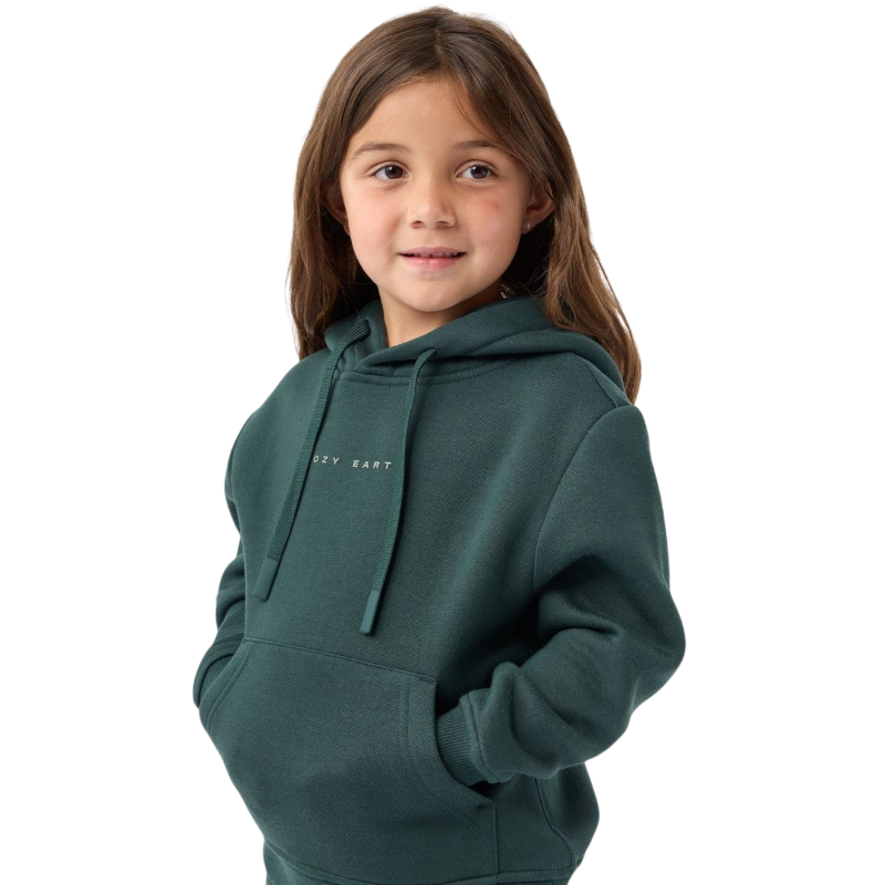 A young girl with long brown hair is wearing a Kid's CityScape Hoodie by Cozy Earth, featuring the brand logo. She has her hands in the hoodie pockets and is smiling slightly, standing against a plain white background. |Color:Spruce