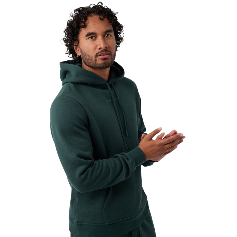 A person with curly hair is wearing a Cozy Earth Men's CityScape Hoodie in dark green and standing against a plain white background, with their hands together. |Color:Spruce