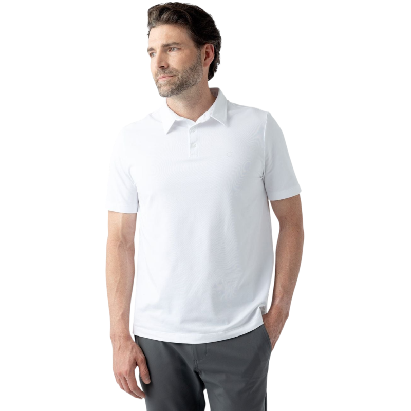 A man with short brown hair, a beard, and mustache is standing against a plain white background. He is wearing the Men's Everyday Polo from Cozy Earth in white and gray pants. One hand is in his pant pocket as he gazes to the side with a neutral expression. |Color:White