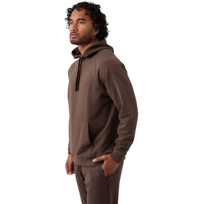 A person wearing the Men's StretchTech Hoodie from Cozy Earth, paired with matching gray pants, stands against a plain white background. The hoodie features drawstrings and a front pocket. The individual is looking forward with a neutral expression. |Color:Coal Heather