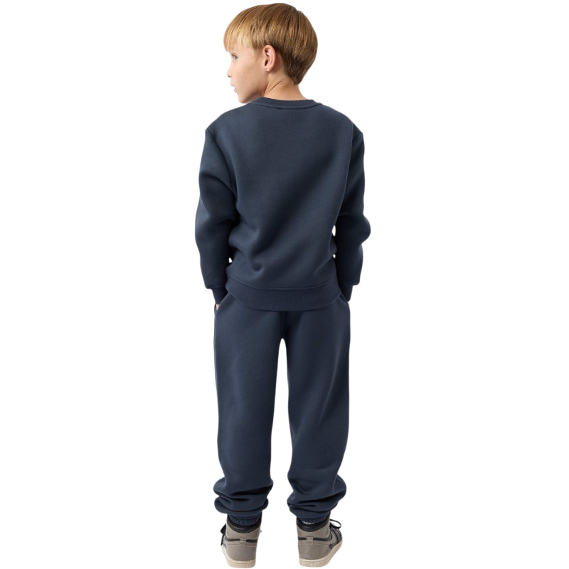 A young boy with blond hair is wearing the Cozy Earth Kid's CityScape Crewneck sweatshirt along with matching pants. He is standing, smiling, and looking slightly to the side against a plain white background. |Color:Eclipse