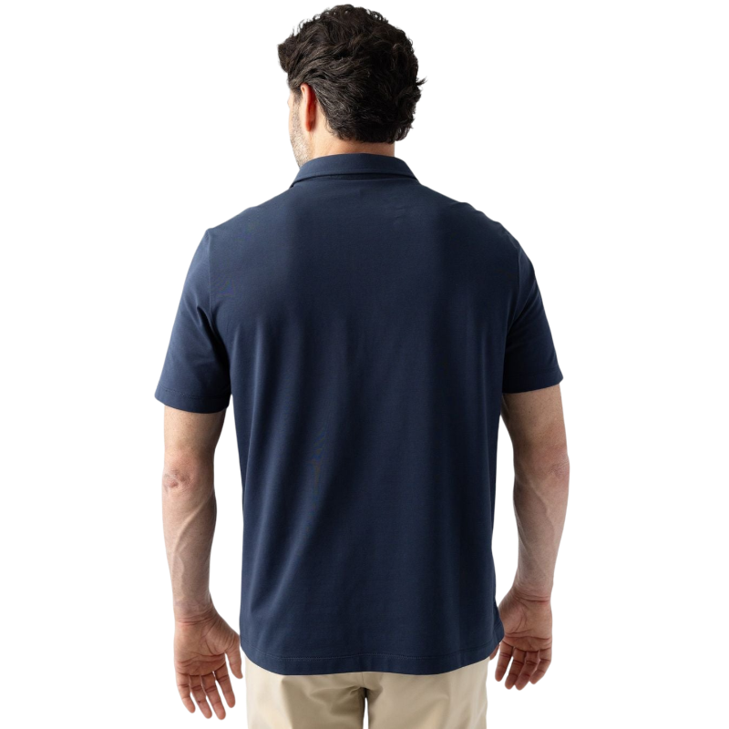 A person with short, light brown hair is wearing the Men's Everyday Polo by Cozy Earth in a light gray shade, paired with light beige pants. They are standing and slightly looking over their left shoulder with a neutral expression against a plain white background. |Color:Stone