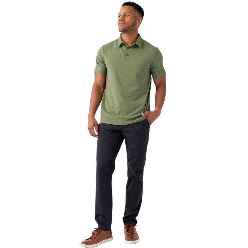 A person with short, light brown hair is wearing the Men's Everyday Polo by Cozy Earth in a light gray shade, paired with light beige pants. They are standing and slightly looking over their left shoulder with a neutral expression against a plain white background. |Color:Stone