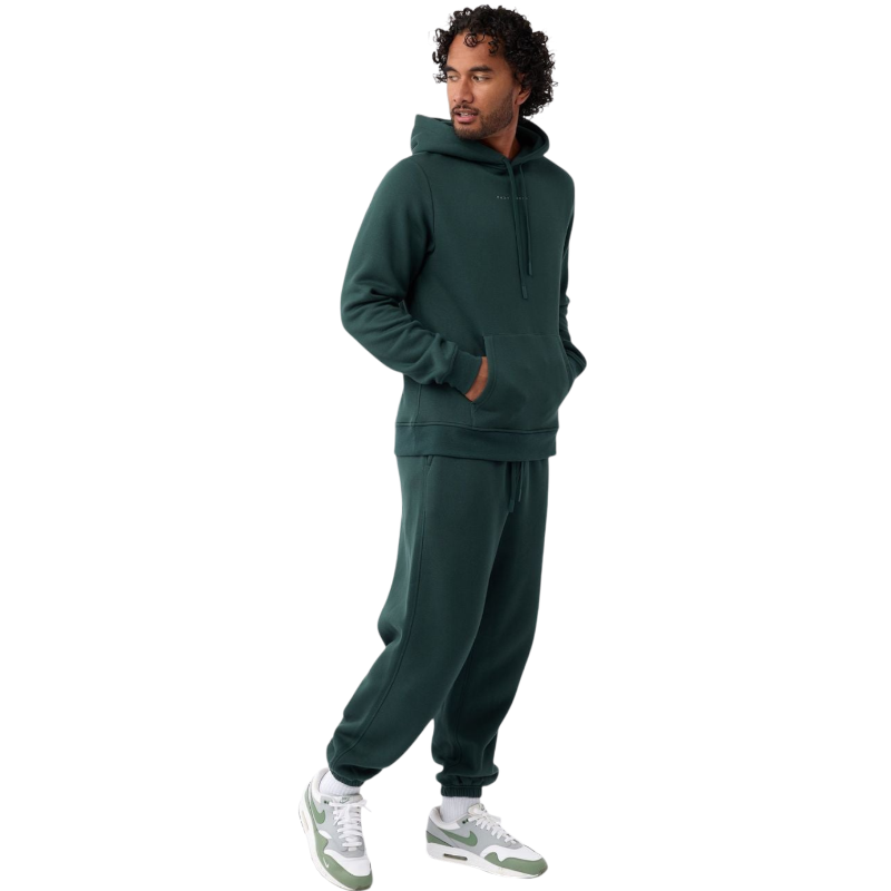A person with curly hair is wearing a Cozy Earth Men's CityScape Hoodie in dark green and standing against a plain white background, with their hands together. |Color:Spruce