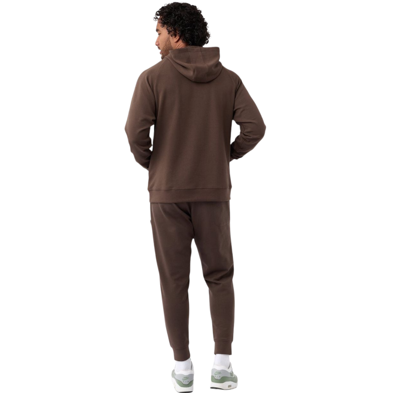 A person wearing the Men's StretchTech Hoodie from Cozy Earth, paired with matching gray pants, stands against a plain white background. The hoodie features drawstrings and a front pocket. The individual is looking forward with a neutral expression. |Color:Coal Heather