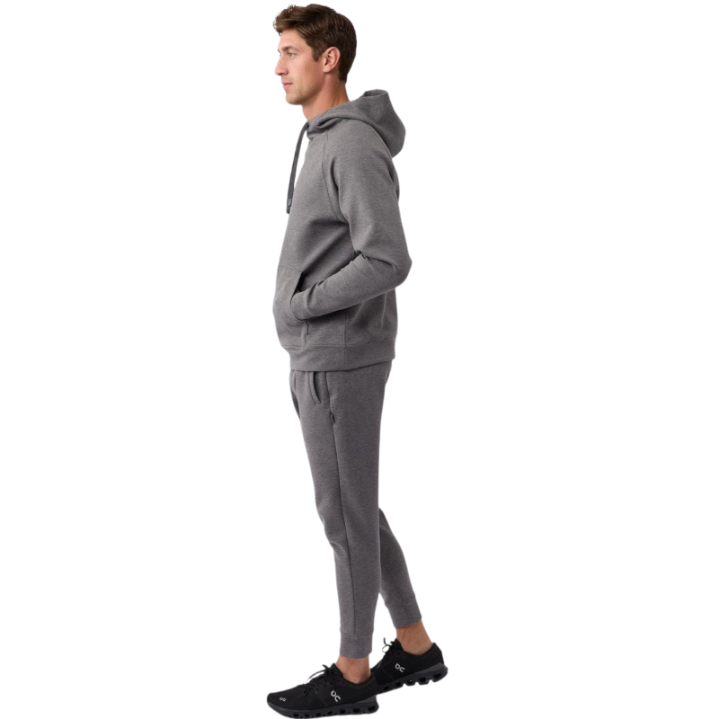 A person wearing the Men's StretchTech Hoodie from Cozy Earth, paired with matching gray pants, stands against a plain white background. The hoodie features drawstrings and a front pocket. The individual is looking forward with a neutral expression. |Color:Coal Heather