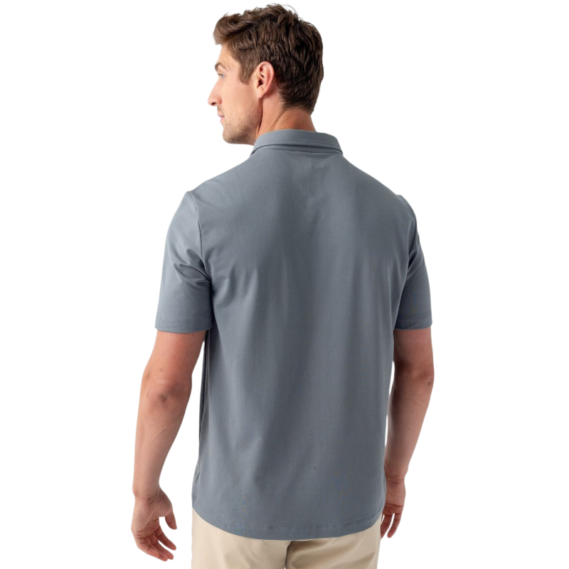 A person with short, light brown hair is wearing the Men's Everyday Polo by Cozy Earth in a light gray shade, paired with light beige pants. They are standing and slightly looking over their left shoulder with a neutral expression against a plain white background. |Color:Stone