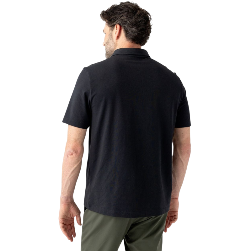 A person with short, light brown hair is wearing the Men's Everyday Polo by Cozy Earth in a light gray shade, paired with light beige pants. They are standing and slightly looking over their left shoulder with a neutral expression against a plain white background. |Color:Stone