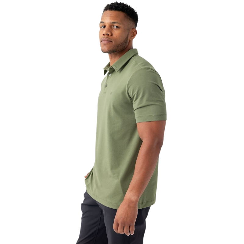 A person with short, light brown hair is wearing the Men's Everyday Polo by Cozy Earth in a light gray shade, paired with light beige pants. They are standing and slightly looking over their left shoulder with a neutral expression against a plain white background. |Color:Stone