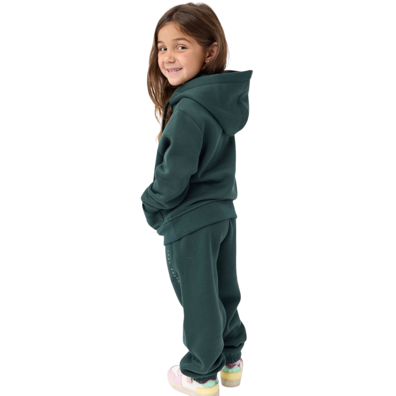 A young child with long blonde hair smiles while wearing a navy blue Kid's CityScape Hoodie by Cozy Earth and matching pants. She has two hair ties, one pink and one blue. The background is plain white. |Color:Eclipse