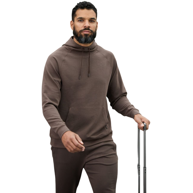 A person wearing the Men's StretchTech Hoodie from Cozy Earth, paired with matching gray pants, stands against a plain white background. The hoodie features drawstrings and a front pocket. The individual is looking forward with a neutral expression. |Color:Coal Heather
