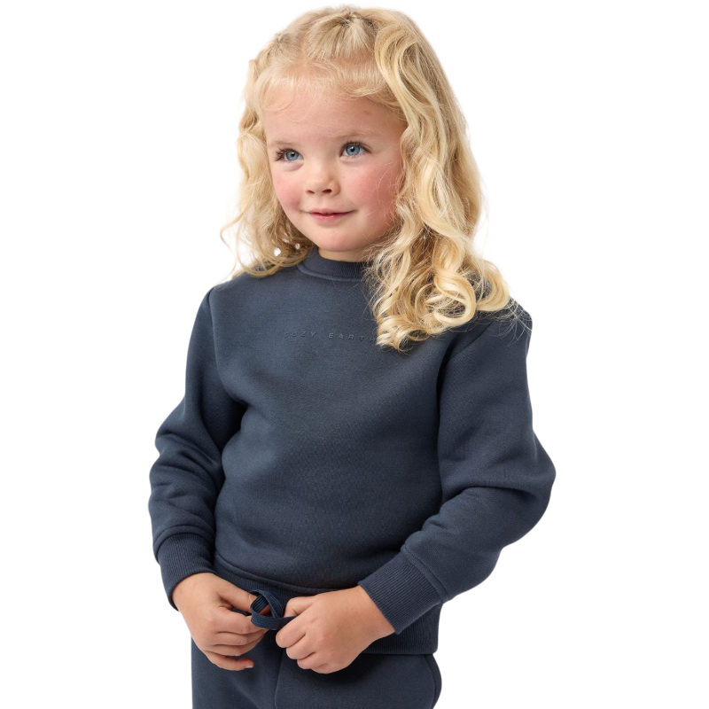 A young boy with blond hair is wearing the Cozy Earth Kid's CityScape Crewneck sweatshirt along with matching pants. He is standing, smiling, and looking slightly to the side against a plain white background. |Color:Eclipse