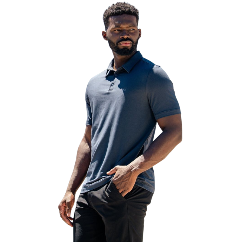 A person with short, light brown hair is wearing the Men's Everyday Polo by Cozy Earth in a light gray shade, paired with light beige pants. They are standing and slightly looking over their left shoulder with a neutral expression against a plain white background. |Color:Stone