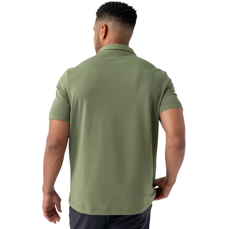 A person with short, light brown hair is wearing the Men's Everyday Polo by Cozy Earth in a light gray shade, paired with light beige pants. They are standing and slightly looking over their left shoulder with a neutral expression against a plain white background. |Color:Stone