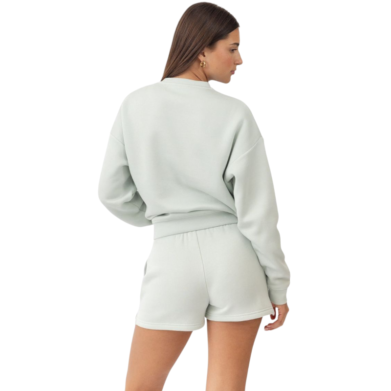 A person with curly hair models the Cozy Earth Women's CityScape Crewneck and matching pants in light pink against a plain white backdrop. |Color:Peony