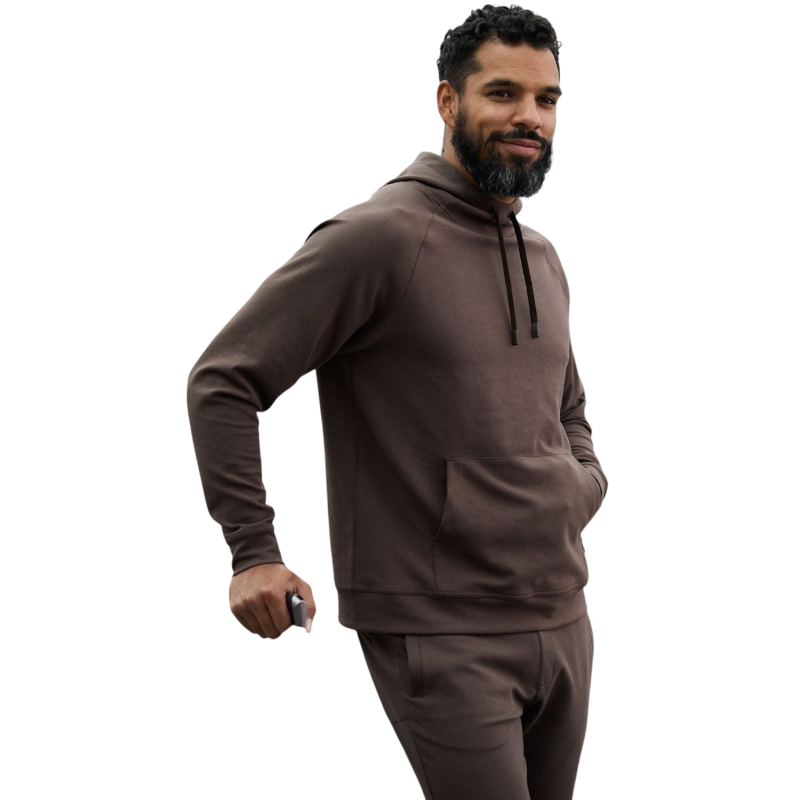 A person wearing the Men's StretchTech Hoodie from Cozy Earth, paired with matching gray pants, stands against a plain white background. The hoodie features drawstrings and a front pocket. The individual is looking forward with a neutral expression. |Color:Coal Heather