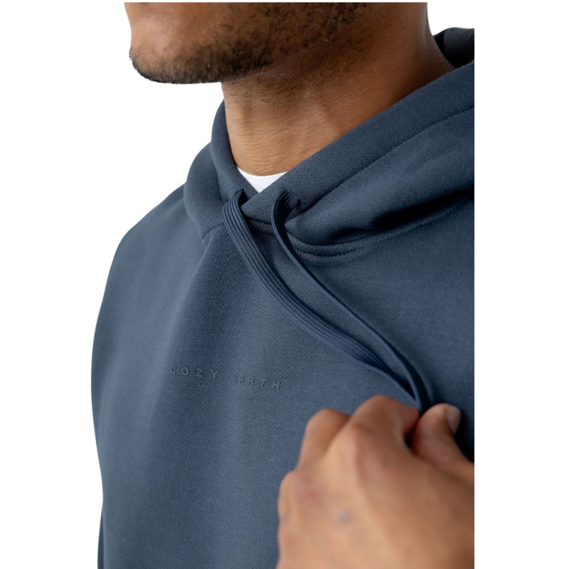 A person with curly hair is wearing a Cozy Earth Men's CityScape Hoodie in dark green and standing against a plain white background, with their hands together. |Color:Spruce