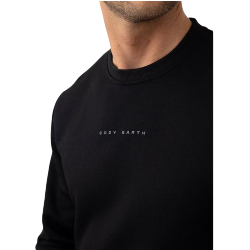 A man with short brown hair is wearing a dark green Men's CityScape Crewneck from Cozy Earth, featuring the words "COLD EARTH" printed on it. He is gazing slightly to the side against a plain white background. |Color:Spruce