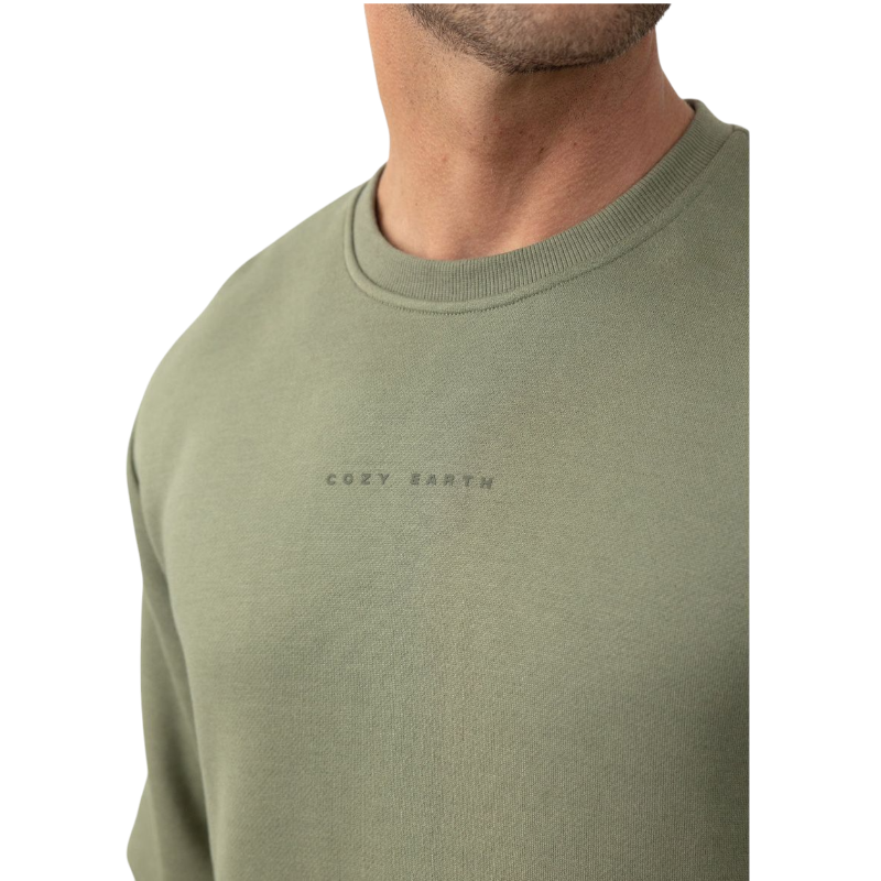 A man with short brown hair is wearing a dark green Men's CityScape Crewneck from Cozy Earth, featuring the words "COLD EARTH" printed on it. He is gazing slightly to the side against a plain white background. |Color:Spruce