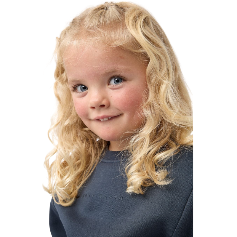 A young boy with blond hair is wearing the Cozy Earth Kid's CityScape Crewneck sweatshirt along with matching pants. He is standing, smiling, and looking slightly to the side against a plain white background. |Color:Eclipse