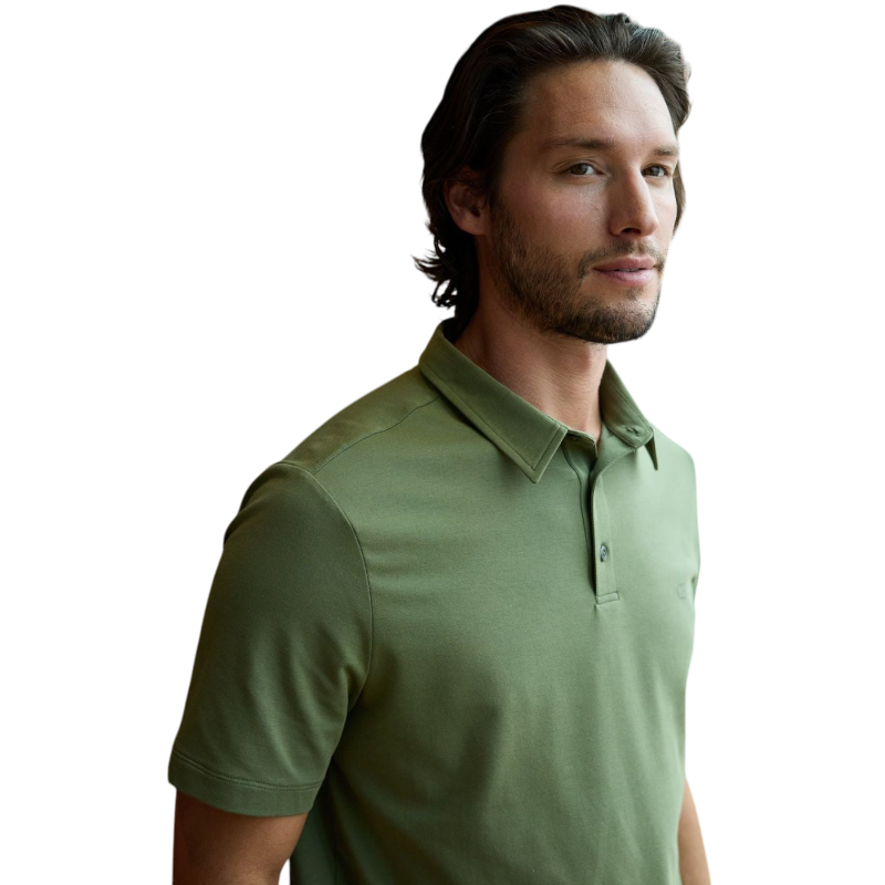A person with short, light brown hair is wearing the Men's Everyday Polo by Cozy Earth in a light gray shade, paired with light beige pants. They are standing and slightly looking over their left shoulder with a neutral expression against a plain white background. |Color:Stone