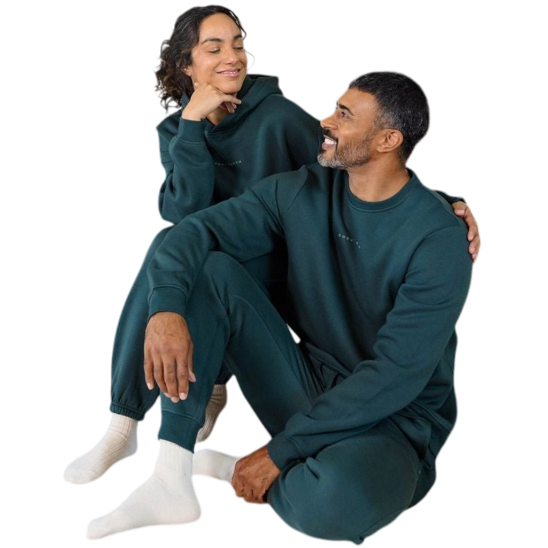 A man with short brown hair is wearing a dark green Men's CityScape Crewneck from Cozy Earth, featuring the words "COLD EARTH" printed on it. He is gazing slightly to the side against a plain white background. |Color:Spruce