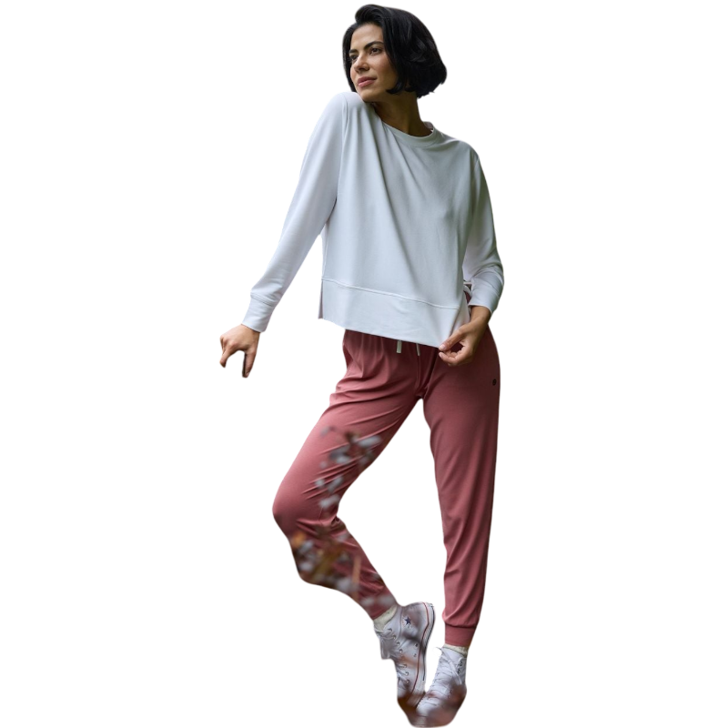 A person with long black hair is standing against a plain white background, wearing a Cozy Earth Women's StudioLite Crewneck in light green and dark green pants. They are looking down with a gentle smile, gently touching their neck with one hand. |Color:Haze