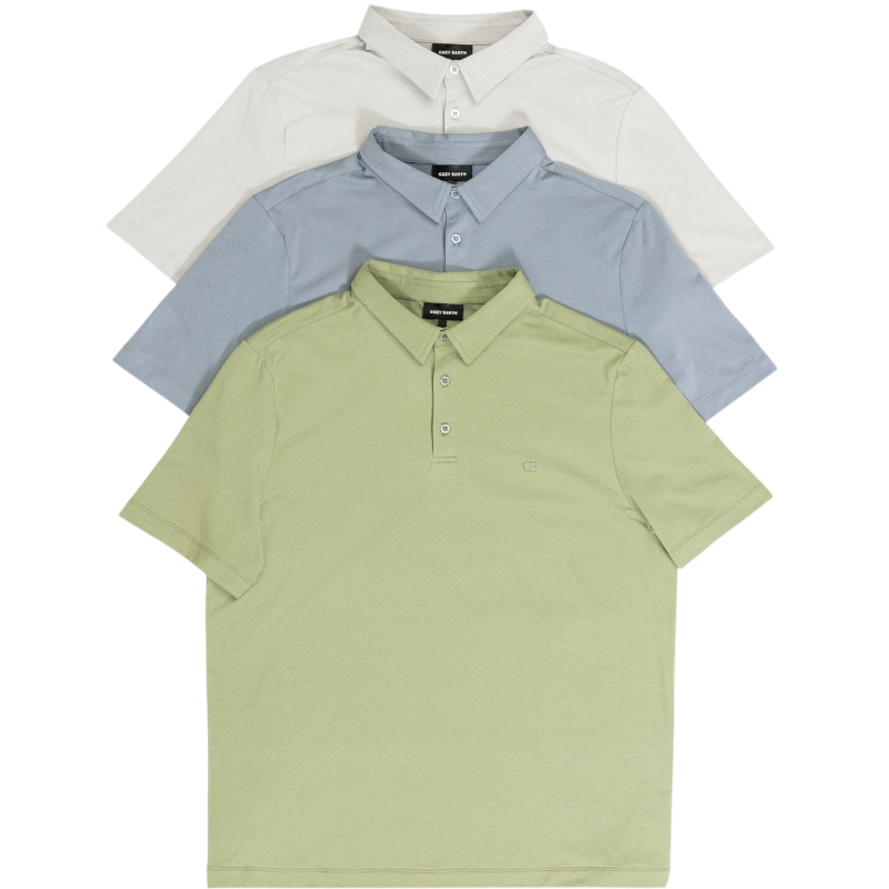 A person with short, light brown hair is wearing the Men's Everyday Polo by Cozy Earth in a light gray shade, paired with light beige pants. They are standing and slightly looking over their left shoulder with a neutral expression against a plain white background. |Color:Stone