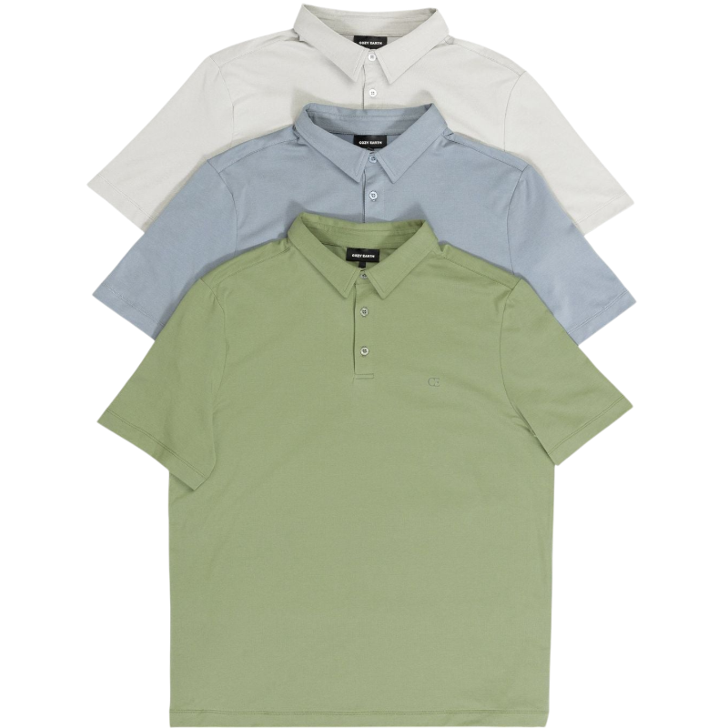 A person with short, light brown hair is wearing the Men's Everyday Polo by Cozy Earth in a light gray shade, paired with light beige pants. They are standing and slightly looking over their left shoulder with a neutral expression against a plain white background. |Color:Stone