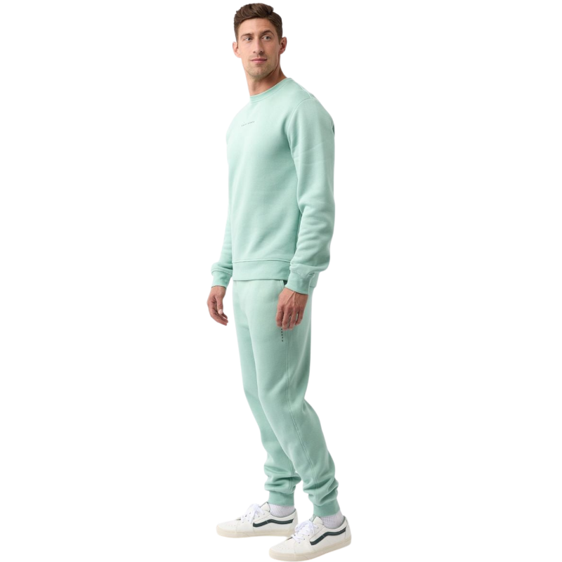 A man with short brown hair is wearing a dark green Men's CityScape Crewneck from Cozy Earth, featuring the words "COLD EARTH" printed on it. He is gazing slightly to the side against a plain white background. |Color:Spruce