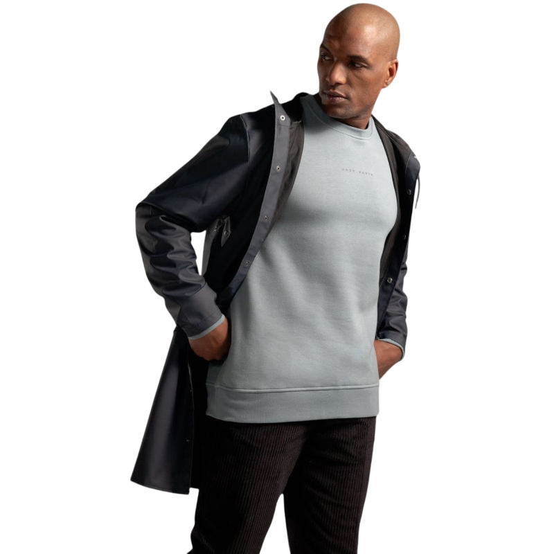 A man with short brown hair is wearing a dark green Men's CityScape Crewneck from Cozy Earth, featuring the words "COLD EARTH" printed on it. He is gazing slightly to the side against a plain white background. |Color:Spruce