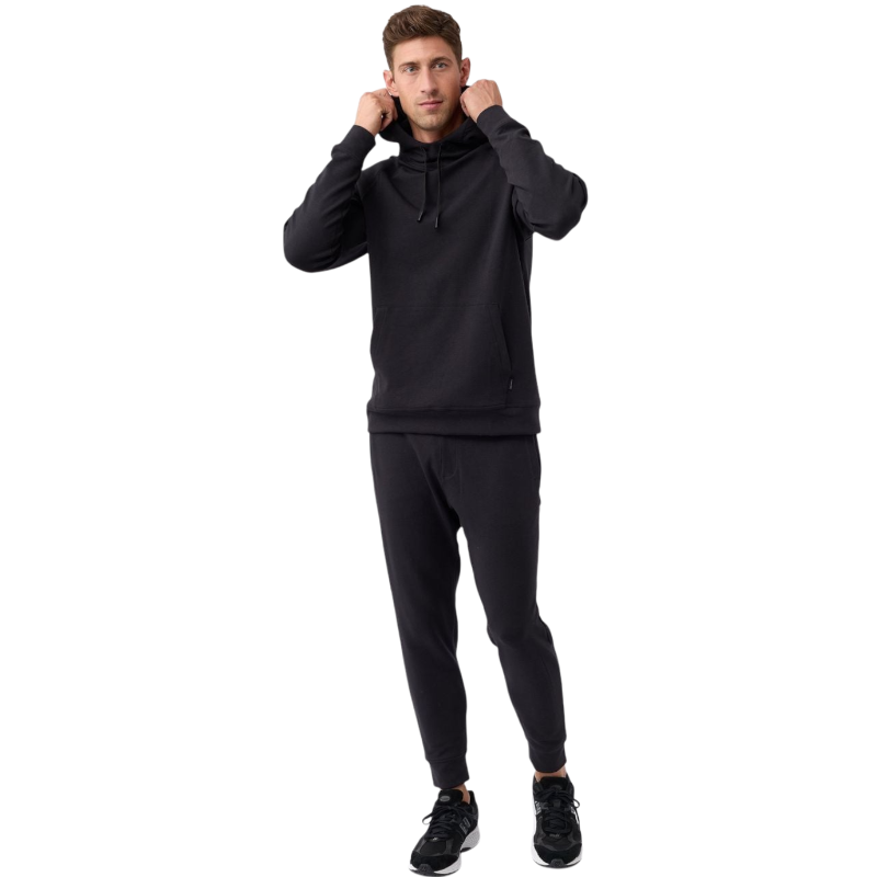 A person wearing the Men's StretchTech Hoodie from Cozy Earth, paired with matching gray pants, stands against a plain white background. The hoodie features drawstrings and a front pocket. The individual is looking forward with a neutral expression. |Color:Coal Heather