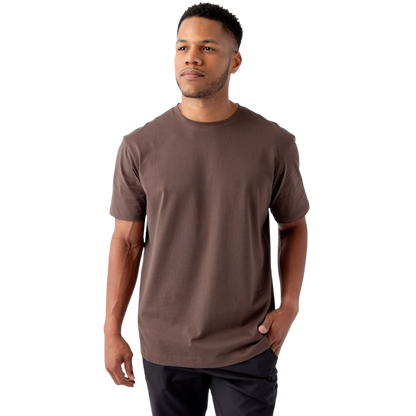 A man with short black hair and a short beard is wearing a brown Men's All Day Tee from Cozy Earth along with black pants. He stands facing slightly to the left with a hand in his pocket, against a plain white background. |Color:Cacao