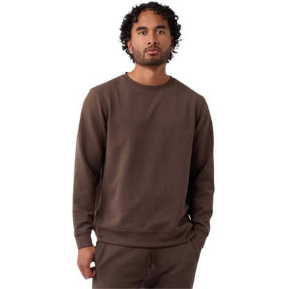 A man with curly hair and a beard wears the Men's StretchTech Crewneck by Cozy Earth in brown, along with matching pants. He stands against a plain white background with his hands in his pockets, looking straight at the camera. |Color:Cacao