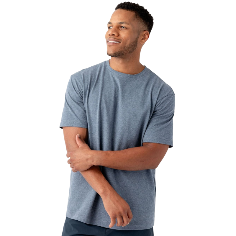 A man wearing the Cozy Earth Men's All Day Tee in plain blue-gray poses against a white background. He has short, dark hair and a beard, and he is smiling while looking off to the side. His left arm is bent, with his hand touching his right arm near the elbow. |Color:Deep Blue Heather