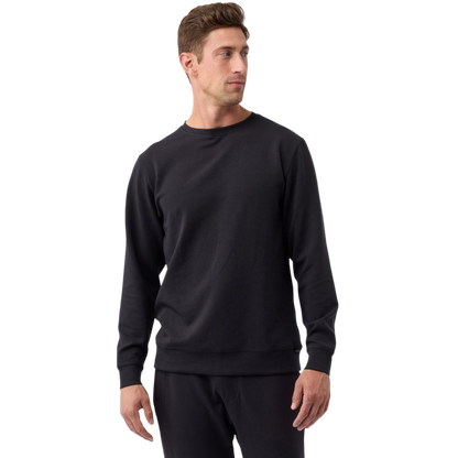 A man with short brown hair, dressed in a Cozy Earth Men's StretchTech Crewneck and black pants, stands against a plain white background. He is looking slightly to his right, with his hands relaxed at his sides. |Color:Jet Black