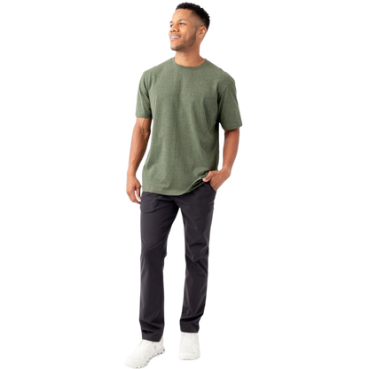 A man is smiling while standing against a plain white background, wearing a Cozy Earth Men's All Day Tee in green, paired with black pants and white sneakers. One of his hands is in his pocket while the other rests relaxed at his side. |Color:Olive Heather