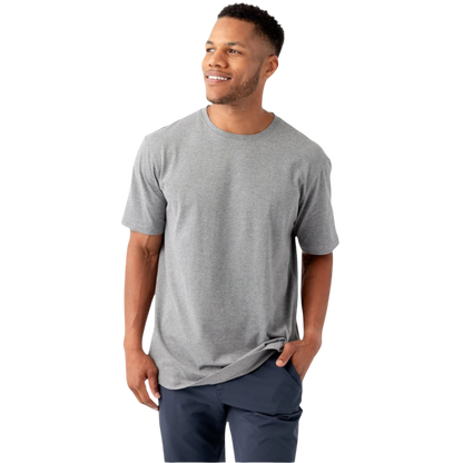 A man stands against a white background, smiling and looking to the side. He is dressed casually in a plain gray Men's All Day Tee by Cozy Earth and dark blue pants. One hand is in his pocket, while the other hangs by his side. |Color:Stone Heather
