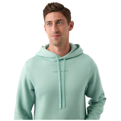A person wearing the Men's CityScape Hoodie by Cozy Earth stands against a plain white background. The light green hoodie features drawstrings and subtle text on the chest. The person, with short brown hair, is looking slightly to the side while smiling gently. |Color:Wintergreen