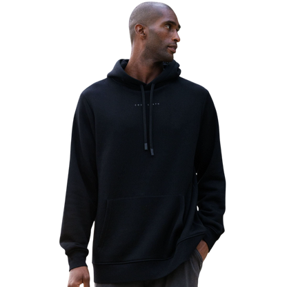 A person with curly hair is wearing a Cozy Earth Men's CityScape Hoodie in dark green and standing against a plain white background, with their hands together. |Color:Spruce