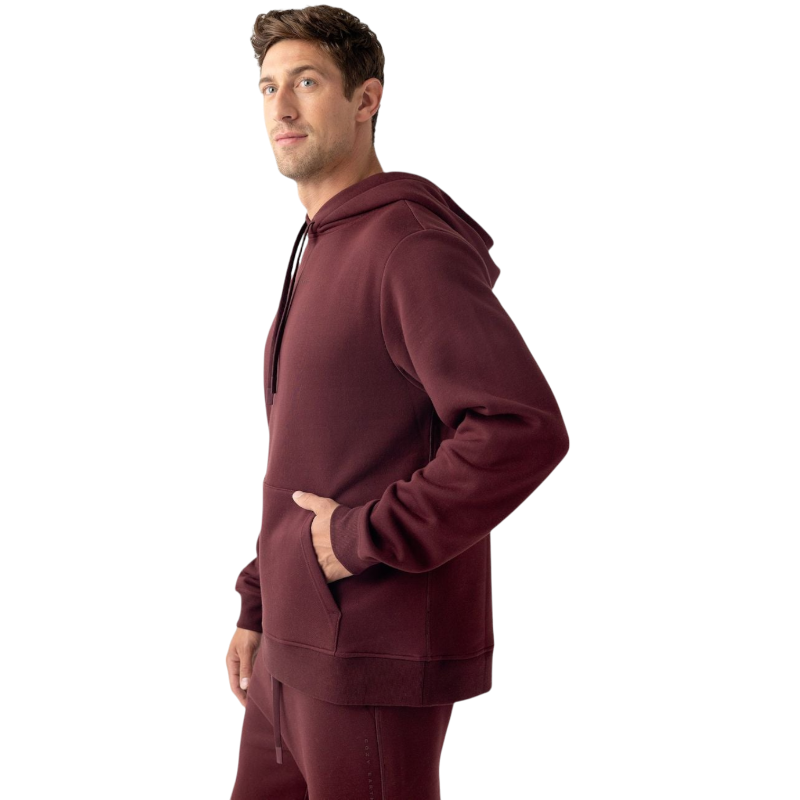 A person with curly hair is wearing a Cozy Earth Men's CityScape Hoodie in dark green and standing against a plain white background, with their hands together. |Color:Spruce