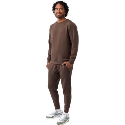 A man is wearing the Men's StretchTech Crewneck sweatshirt from Cozy Earth, paired with matching sweatpants. He stands against a plain white background with short brown hair, looking forward with a neutral expression. |Color:Coal Heather