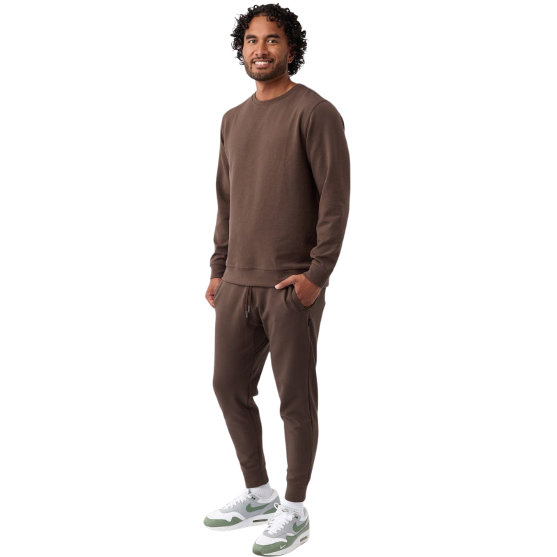 A man is wearing the Men's StretchTech Crewneck sweatshirt from Cozy Earth, paired with matching sweatpants. He stands against a plain white background with short brown hair, looking forward with a neutral expression. |Color:Coal Heather